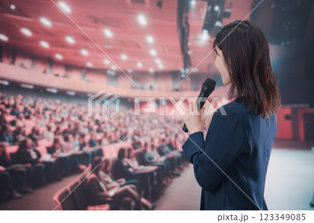 大勢の聴衆が集まるホールで司会をする若い女性 大勢の聴衆が集まるホールで司会をする若い女性 123349085