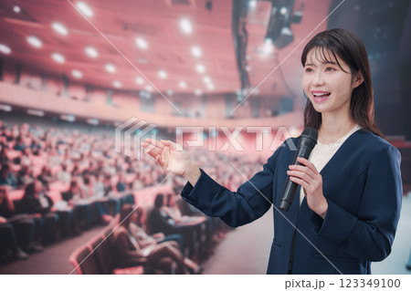 大勢の聴衆が集まるホールで司会をする若い女性 123349100