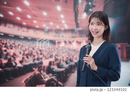 大勢の聴衆が集まるホールで司会をする若い女性 123349102