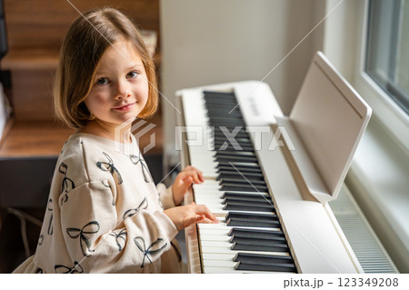 Home lesson on music for the girl on white piano synthesizer. Concept of early development: learning music enhances motor skills, hearing, and intelligence, fostering creativity from childhood Home lesson on music for the girl on white piano synthesizer. Concept of early development: learning music enhances motor skills, hearing, and intelligence, fostering creativity from childhood 123349208