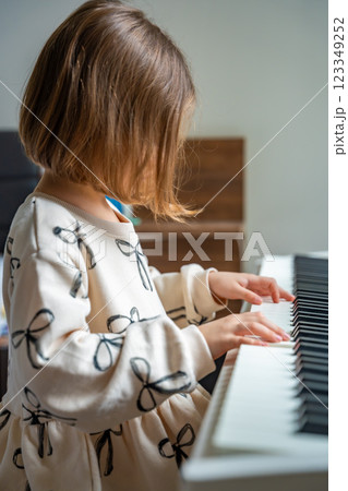 Home lesson on music for the girl on white piano synthesizer. Concept of early development: learning music enhances motor skills, hearing, and intelligence, fostering creativity from childhood Home lesson on music for the girl on white piano synthesizer. Concept of early development: learning music enhances motor skills, hearing, and intelligence, fostering creativity from childhood 123349252