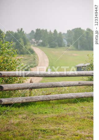 Weathered wooden fence bordering rustic dirt path winding through serene rural russian landscape Weathered wooden fence bordering rustic dirt path winding through serene rural russian landscape 123349447