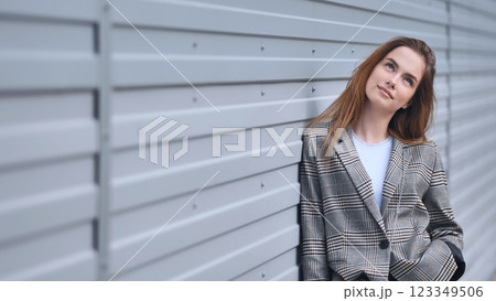 Stylish businesswoman in checkered jacket looking up, contemplating new opportunities, leaning against a modern metal wall 123349506