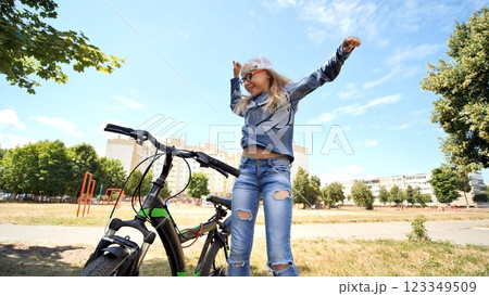 Cheerful schoolgirl dancing beside bicycle, celebrating summer freedom in urban park setting 123349509