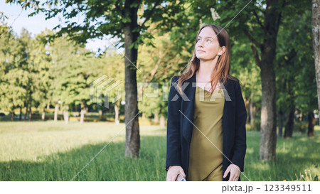 Young businesswoman walking in a green park during her break, enjoying the fresh air and looking up at the trees 123349511