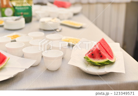 There are pieces of watermelon and clean white cups on the table. 123349571