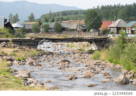 Weathered wooden bridge spanning rocky river between mountain slopes, connecting secluded village nestled amid verdant landscape Weathered wooden bridge spanning rocky river between mountain slopes, connecting secluded village nestled amid verdant landscape 123349584