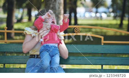 Caring mother comforting weeping child on park bench during bright summer afternoon Caring mother comforting weeping child on park bench during bright summer afternoon 123349720