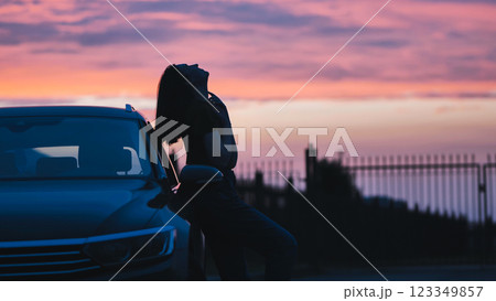 Woman silhouetted against sunset, resting on vehicle with scenic landscape background Woman silhouetted against sunset, resting on vehicle with scenic landscape background 123349857