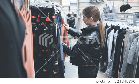 Young shopper browsing fashion store, delicately touching stylish garment on rack, carefully examining potential clothing choice 123349870