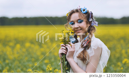 Model wearing white dress and butterfly decorations holding rapeseed bouquet in a yellow field during a cloudy day 123350004