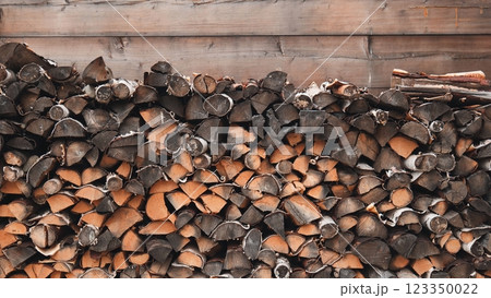 Seasoned firewood stacking densely against weathered wooden wall, creating rustic texture 123350022
