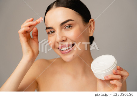 Smiling Woman Applying Face Cream Skincare With a Cream Container 123350156