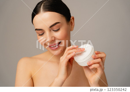 Smiling Woman Applying Cream From Jar With Healthy Skin and Minimalist Background 123350242