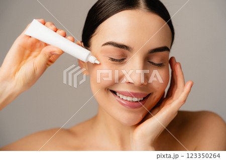 Smiling Woman Applying Skincare Cream to Face with a White Background 123350264
