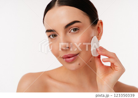 Young Woman Cleansing Her Skin With Cotton Pad in Minimalistic Setting Young Woman Cleansing Her Skin With Cotton Pad in Minimalistic Setting 123350339