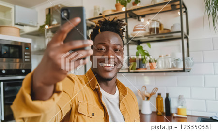 cheerful black african american man making selfie photo for social media, smiling person takes joyful picture in cozy kitchen, radiating friendliness and comfort in modern home setting 123350381
