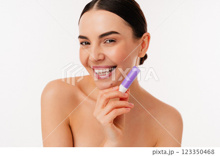 Smiling Bare-Skinned Model Holding a Purple Lip Balm Against White Background 123350468