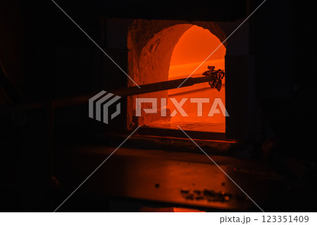 Molten glass on a blowpipe is inside of an open furnace, glass blowing 123351409