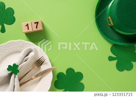 St Patrick's Day and 17 March frame with white plate and traditional decoration, shamrock, clover leaves and green coins on light green background. View from above. Festive invitation. St Patrick's Day and 17 March frame with white plate and traditional decoration, shamrock, clover leaves and green coins on light green background. View from above. Festive invitation. 123351715
