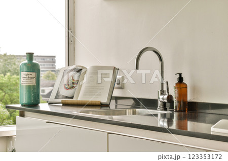 A modern kitchen counter featuring an elegant sink, stacked books, and decorative bottles, illuminated by natural light streaming through a window. 123353172