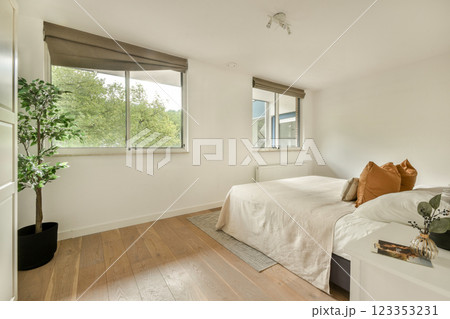 A serene, contemporary bedroom featuring a large window with greenery outside, light-colored walls, and stylish furnishings, creating a calming atmosphere. 123353231