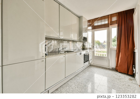 A sleek and modern kitchen with white cabinetry, stainless steel appliances, and large windows providing natural light. The design emphasizes simplicity and functionality. 123353282