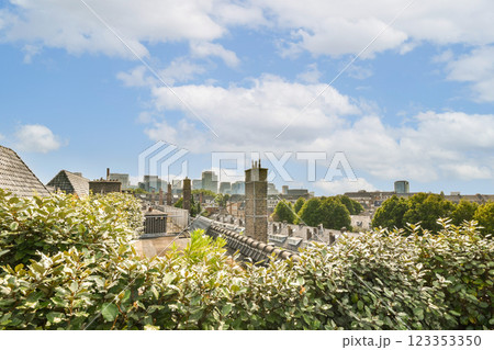 A panoramic view of the city skyline featuring modern buildings framed by lush greenery under a bright blue sky with fluffy clouds. 123353350