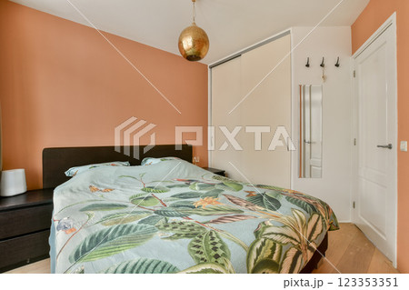 A modern bedroom featuring a cozy bed adorned with a leafy comforter, warm wall colors, and minimalist decor for a relaxing atmosphere. A modern bedroom featuring a cozy bed adorned with a leafy comforter, warm wall colors, and minimalist decor for a relaxing atmosphere. 123353351