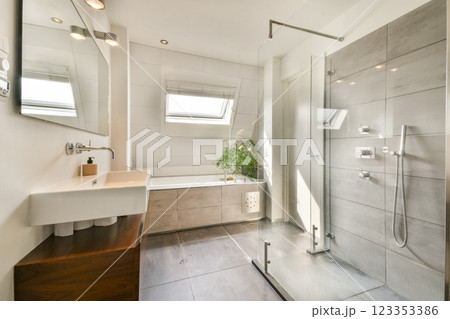 A sleek and modern bathroom featuring a glass shower, stylish fixtures, and natural lighting from a skylight adds elegance to the space. 123353386