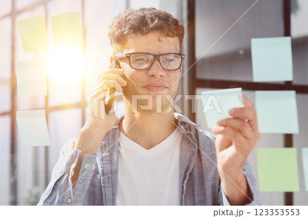 business man standing in front of stickers glass wall and write task on sticker at his office place business man standing in front of stickers glass wall and write task on sticker at his office place 123353553