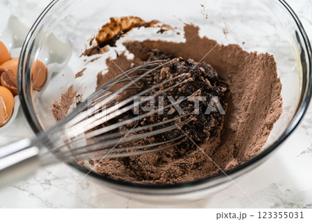 In the process of creating mouthwatering chocolate cupcakes, the first step involves meticulously mixing the ingredients in a glass mixing bowl to make the perfect batter. 123355031
