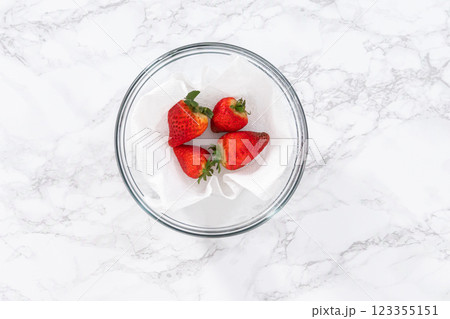 Bright red strawberries, interspersed with signs of mold, rest in a glass bowl lined with a paper towel on a white napkin, indicating improper storage techniques. Bright red strawberries, interspersed with signs of mold, rest in a glass bowl lined with a paper towel on a white napkin, indicating improper storage techniques. 123355151