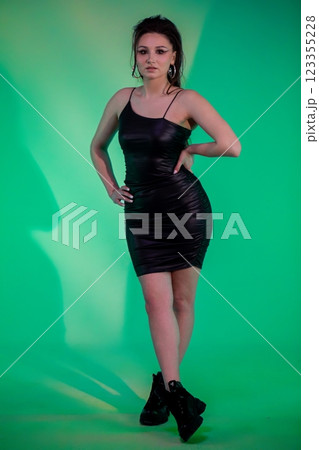 A Stylish Model Elegantly Poses in a Chic Black Dress Set Against a Vibrant Green Background A Stylish Model Elegantly Poses in a Chic Black Dress Set Against a Vibrant Green Background 123355228
