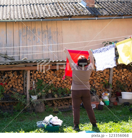 Woman hanging laundry outside on a sunny day, surrounded by nature. Simple domestic scene. Rural setting, laundry drying. 123356068