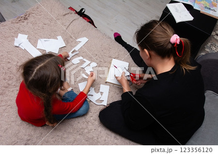 Mother and daughter creating paper crafts together on the floor, enjoying a creative activity in a cozy home environment. Mother and daughter creating paper crafts together on the floor, enjoying a creative activity in a cozy home environment. 123356120