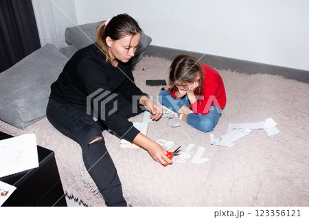 Mom and daughter crafting together: bonding while cutting paper on the bed. Making memories during a creative family time at home. Mom and daughter crafting together: bonding while cutting paper on the bed. Making memories during a creative family time at home. 123356121