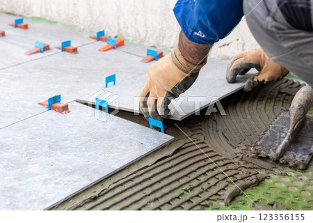 Tiler at work installing new floor with tiles. Construction. 123356155