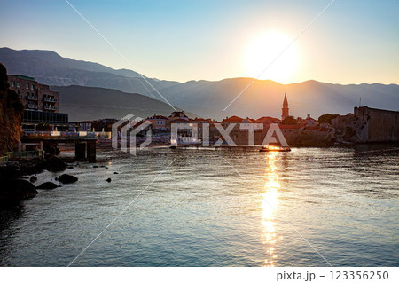 Sunset glows over a tranquil bay with the charming old town of Budva set against a backdrop of majestic mountains. 123356250