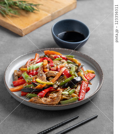 Stir-fry with vegetables and meat on dark background with chopsticks, glass of water and soy sauce. 123356311
