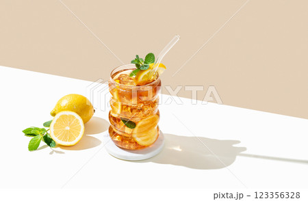 Iced tea with lemon, ice and mint in a glass on beige and white background with shadow 123356328