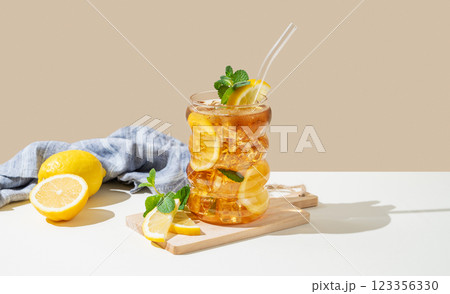 Iced tea with lemon, ice and mint in a glass on beige and white background with shadow 123356330