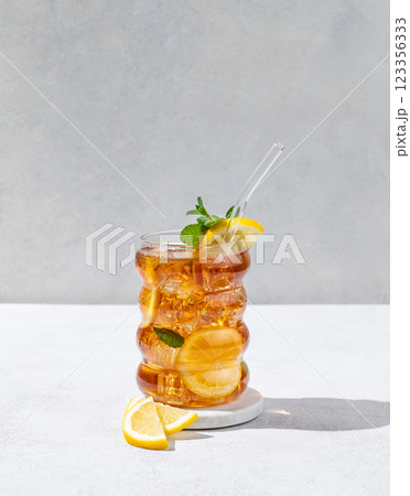Iced tea with lemon, ice and mint in a glass on light texture background with shadow. Iced tea with lemon, ice and mint in a glass on light texture background with shadow. 123356333