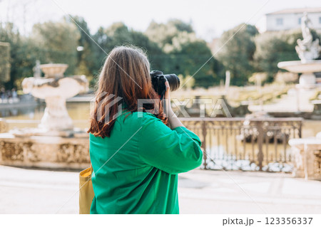 Happy 30s Woman photographer with a professional camera takes pictures on old town background. Home hobby, lifestyle, travel, people concept. 123356337