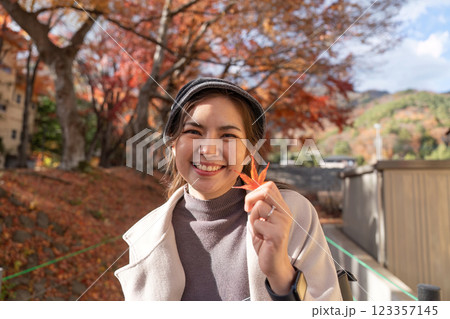 Smiling Asian Woman Enjoying Autumn Holding a Maple Leaf 123357145
