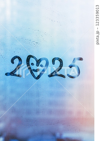 Doodle numbers 2025 of new year with heart shape smile paint on foggy glass on blue window Doodle numbers 2025 of new year with heart shape smile paint on foggy glass on blue window 123359013