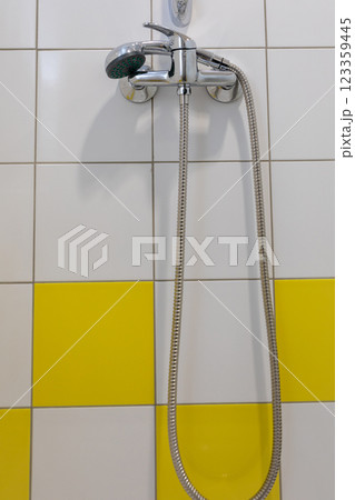 A modern showerhead complements the bright, inviting yellow tiled wall in a stylish bathroom A modern showerhead complements the bright, inviting yellow tiled wall in a stylish bathroom 123359445
