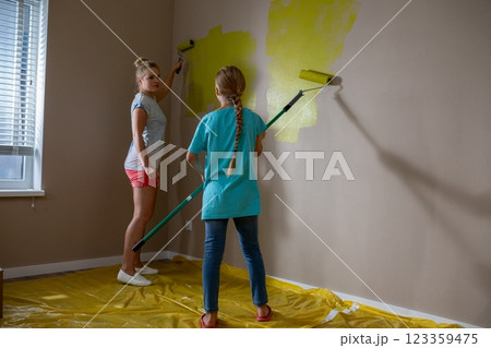 Two Young Children Thoroughly Enjoy Painting a Wall with a Bright, Cheerful Yellow Color 123359475