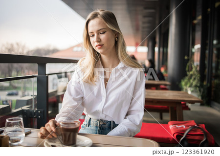 Gen z blonde woman drinks hot chocolate in summer cafe. Tasty beverage and break concept. Generation z people 123361920