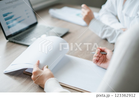 Professionals engaged in a business meeting, reviewing documents and analyzing data on a laptop in a modern office environment. 123362912